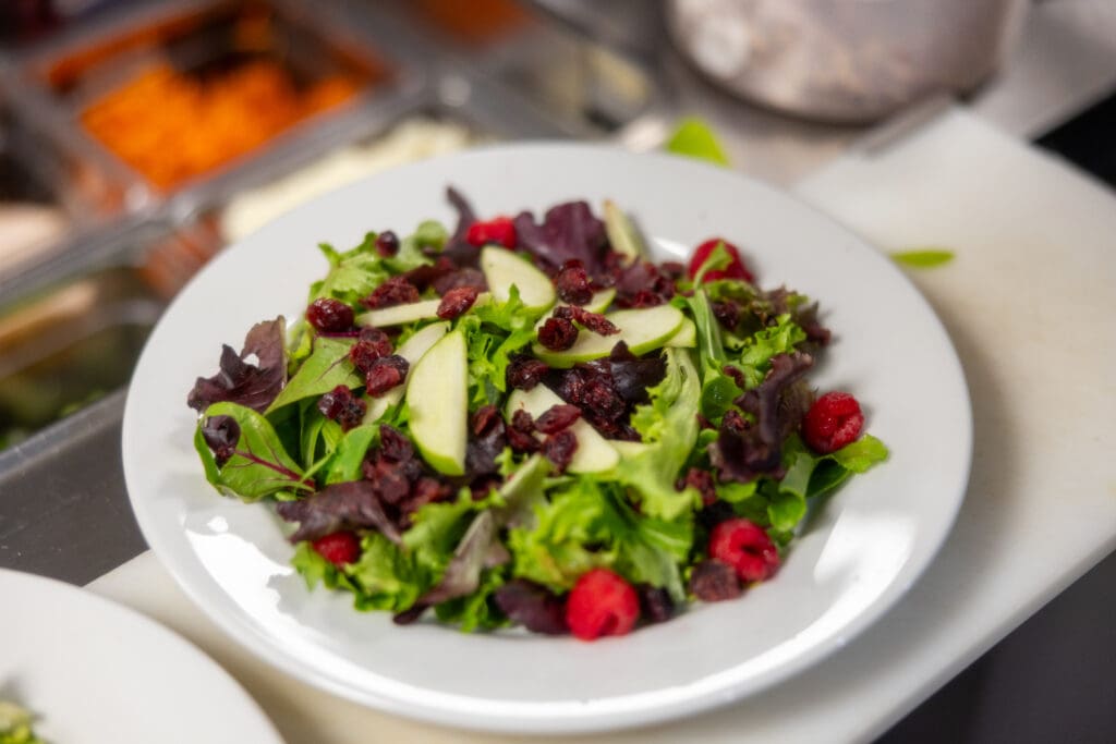 A salad from the senior living dining experience at Clarendale Arcadia in Phoenix, AZ. The Salad features dried cranberries, raspberries, sliced green apples, and spinach, all foods part of a Blue Zone diet for seniors.